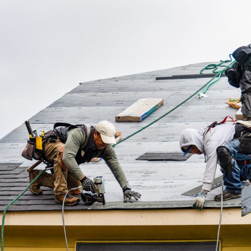 crew installing new shingles on roof on a rainy day